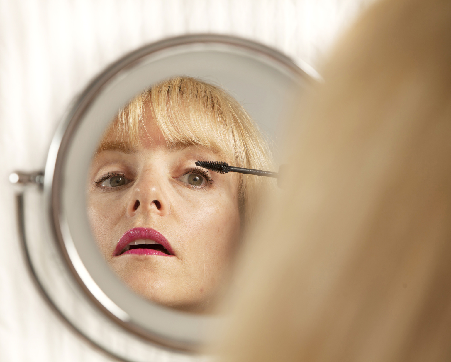 Attractive blond woman applies eyeliner makeup in mirror