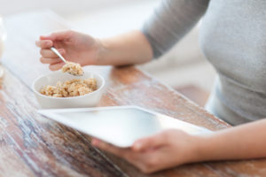 woman eating porridge and using tablet pc