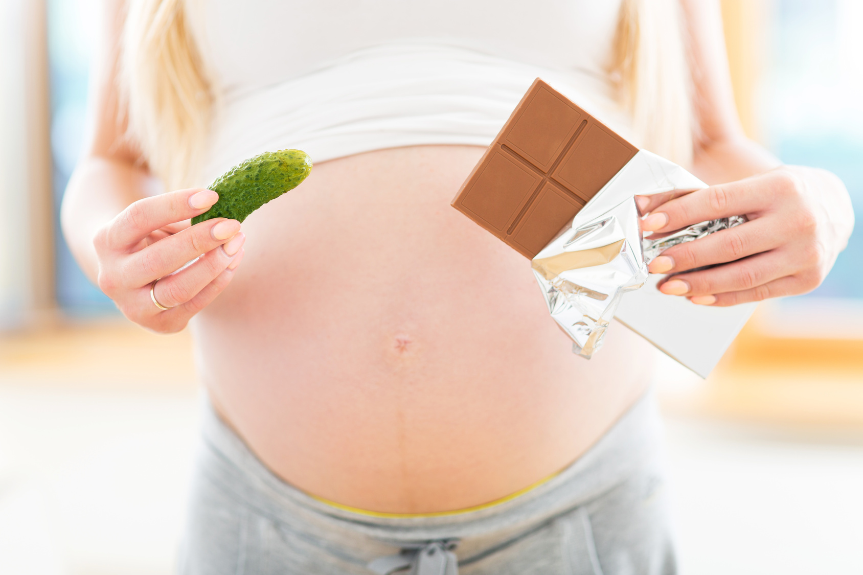Pregnant woman holding pickle and chocolate