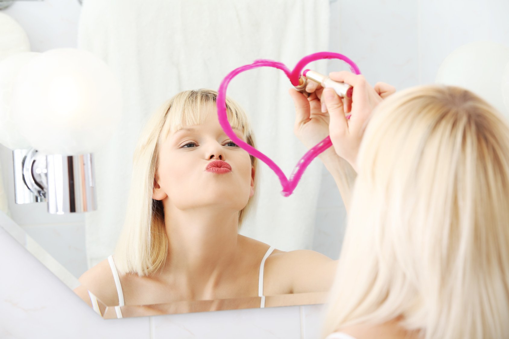 Young woman drawing big heart on mirror.