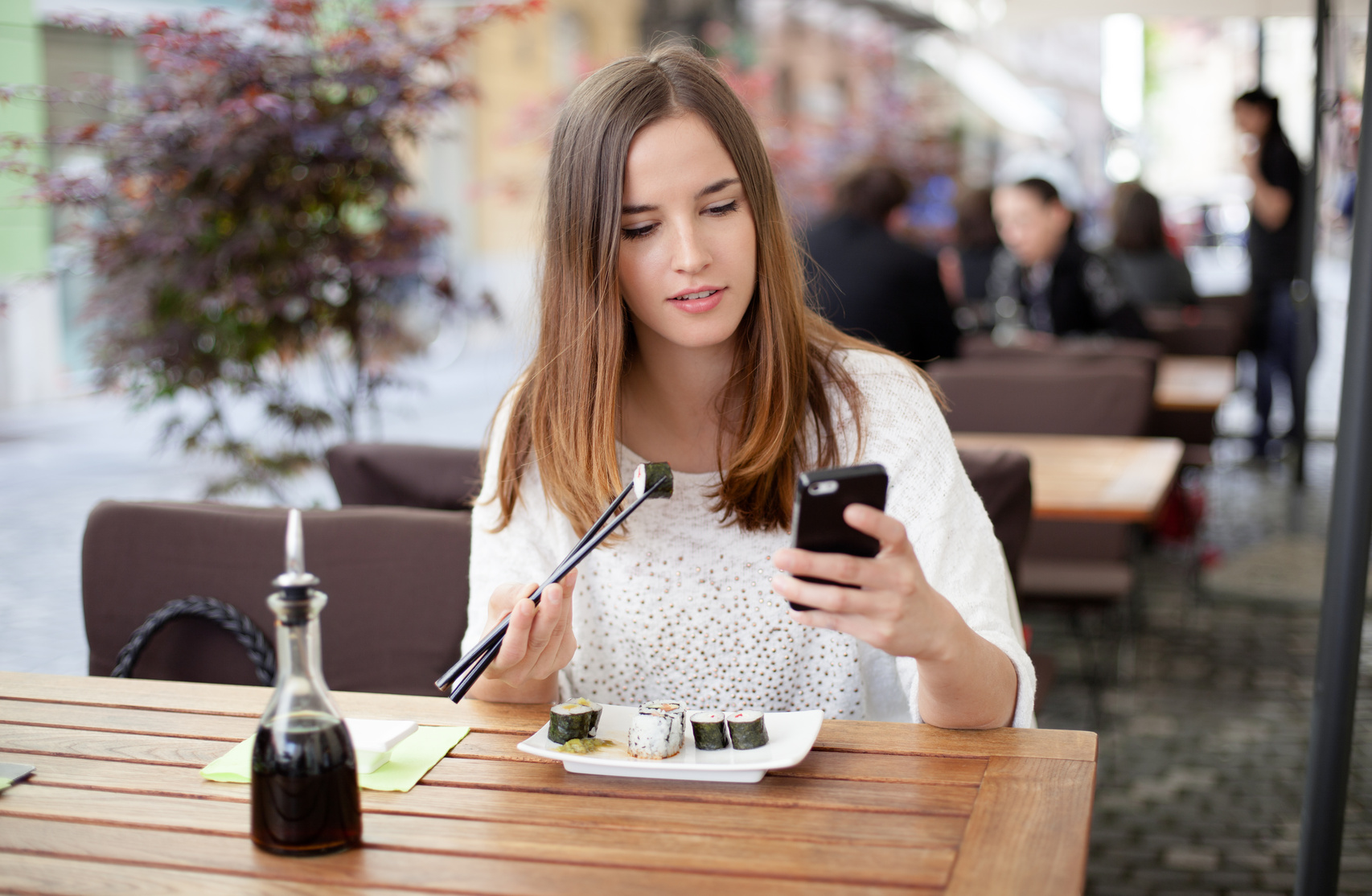 Young woman reading a message while eating sushi in a restaurant