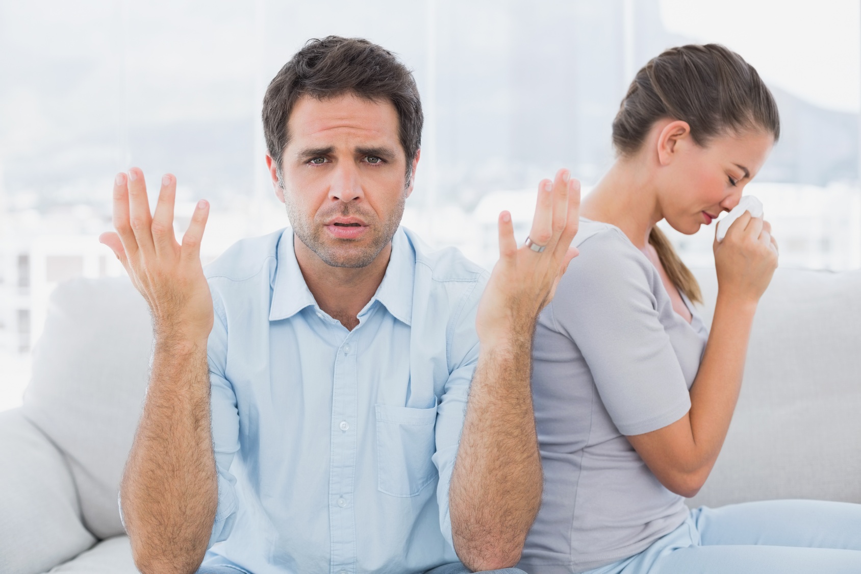 Man gesturing at camera with his crying partner on the couch