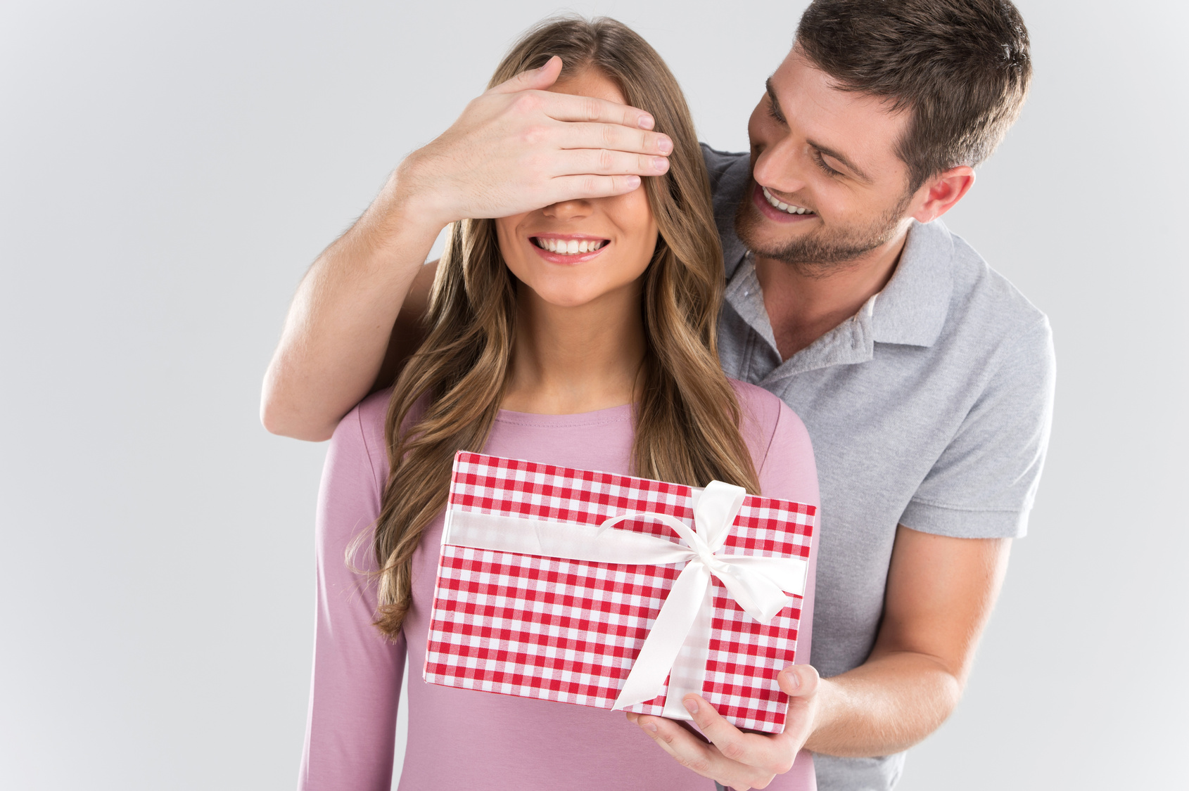 Man surprising his girlfriend with gift on grey background.