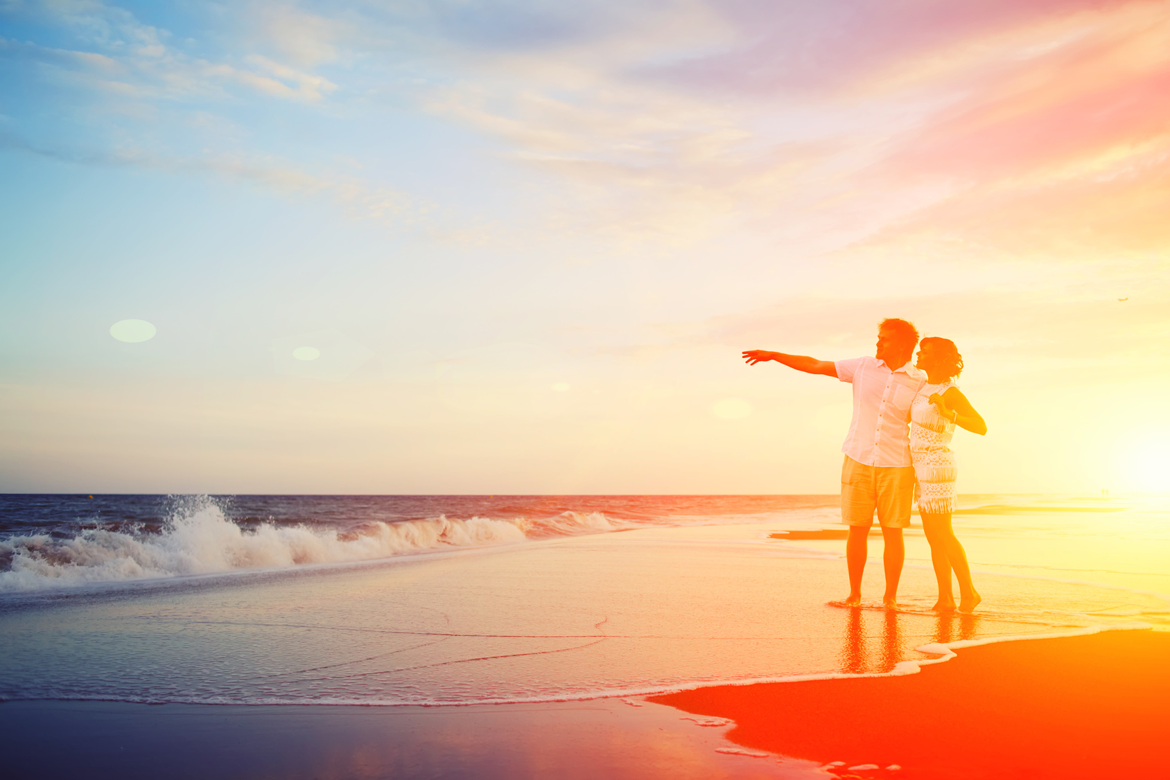 Happy young couple embracing enjoying ocean sunset