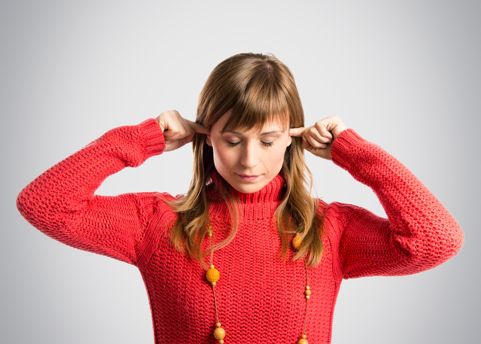 Young pretty woman covering her ears over grey background