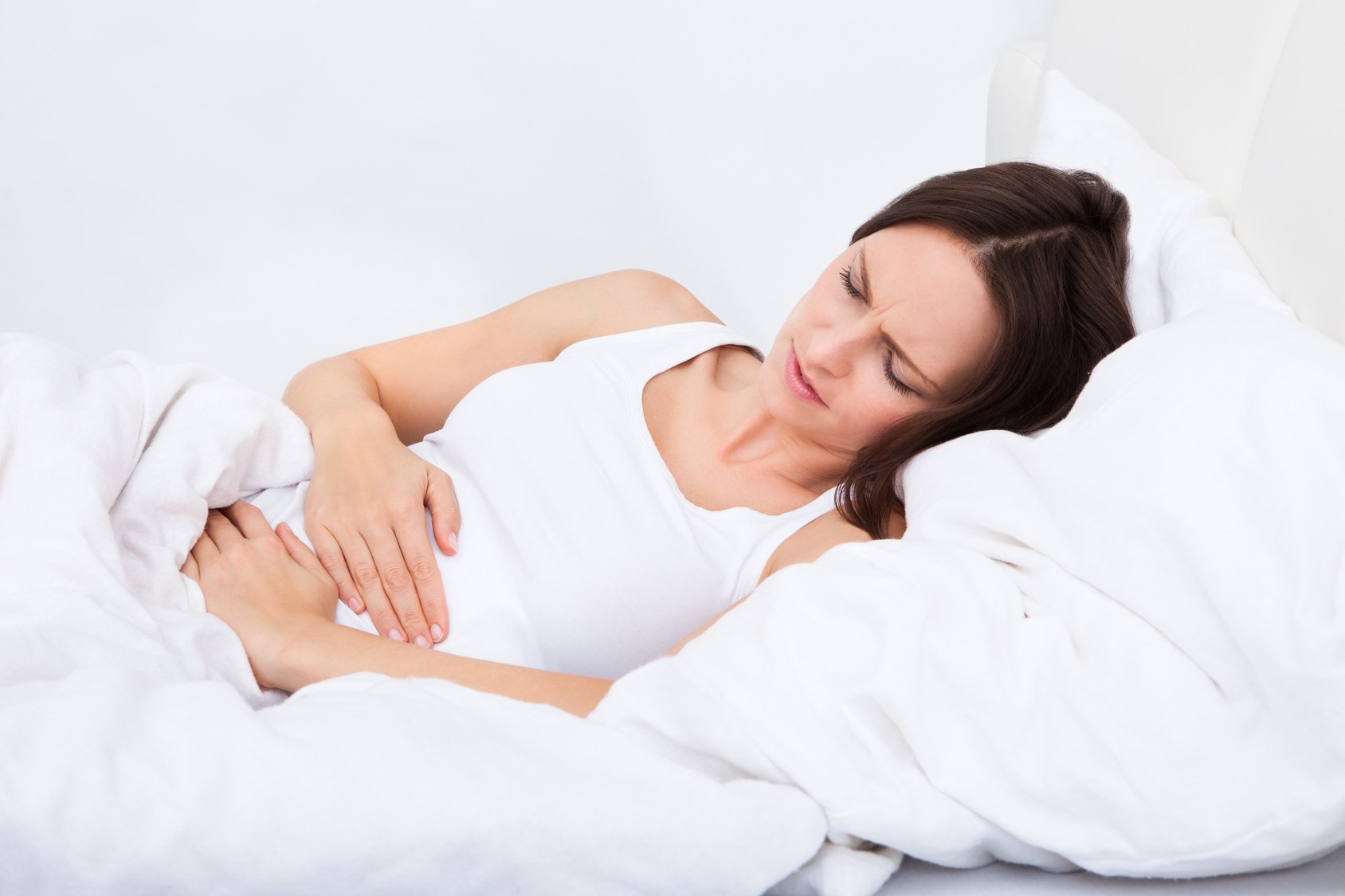 Woman with stomach ache lying on bed