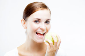 Smiling woman holding and eating green apple