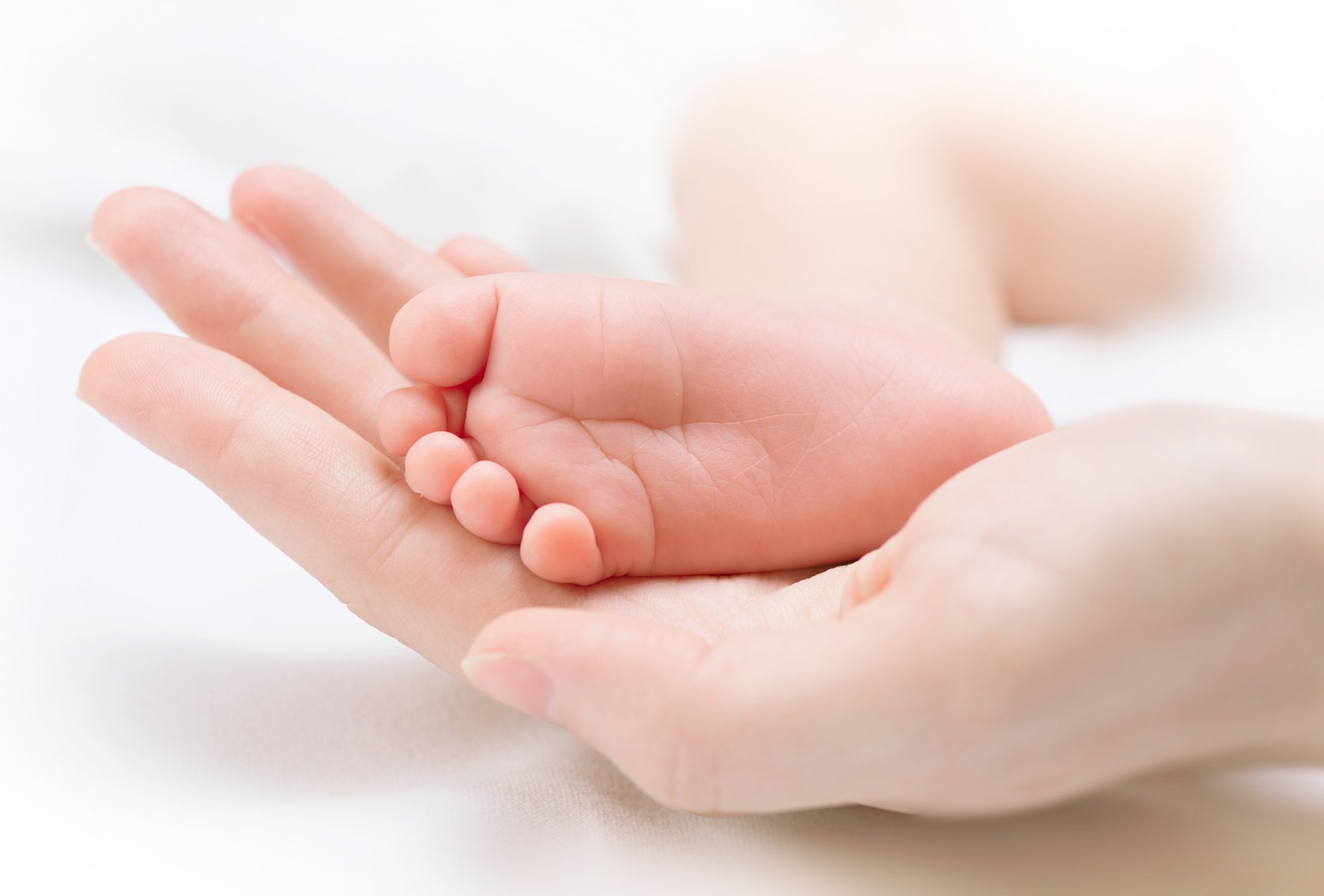 Tiny newborn baby’s foot on female hands closeup