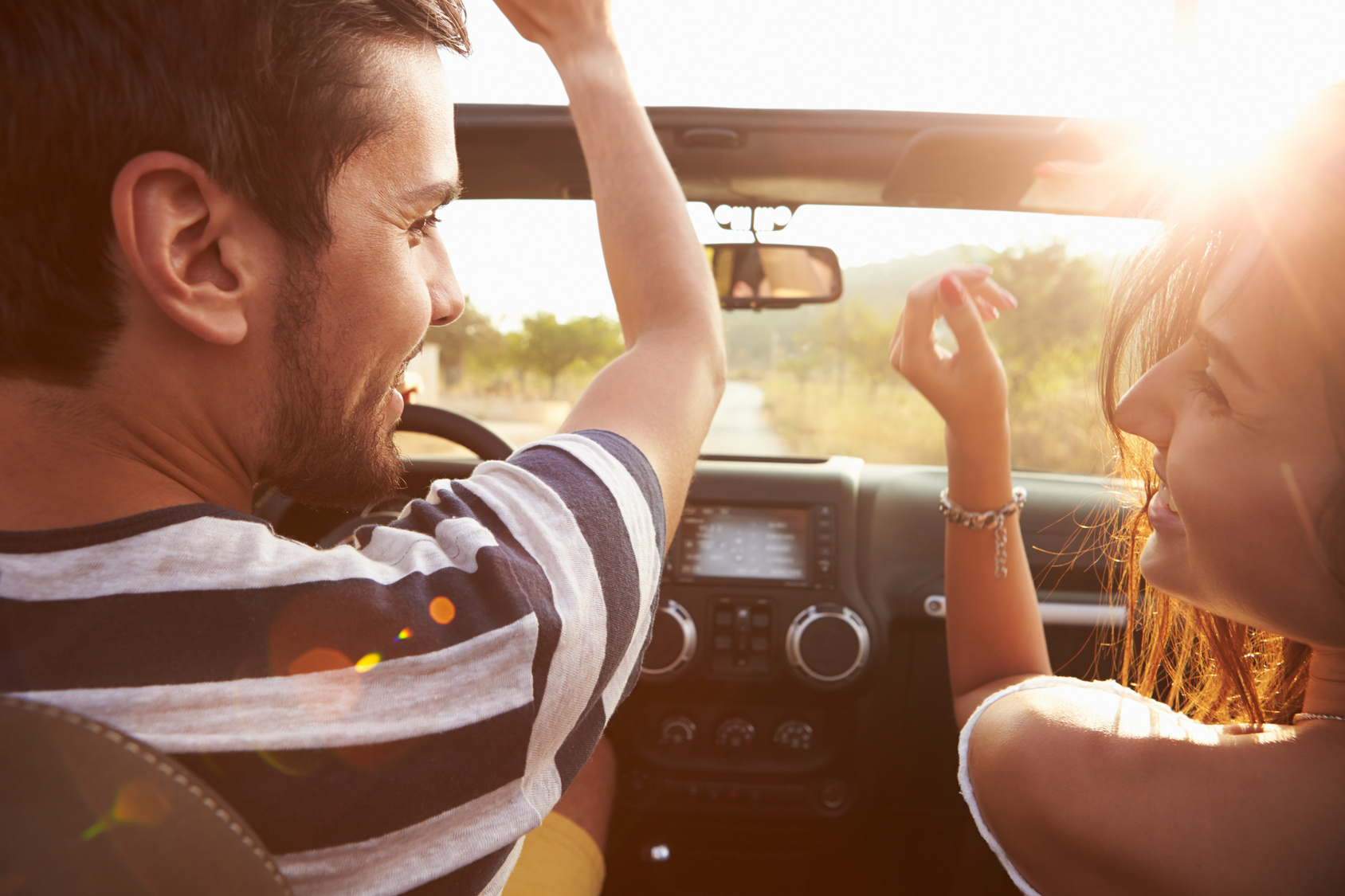 Young Couple Driving Along Country Road In Open Top Car