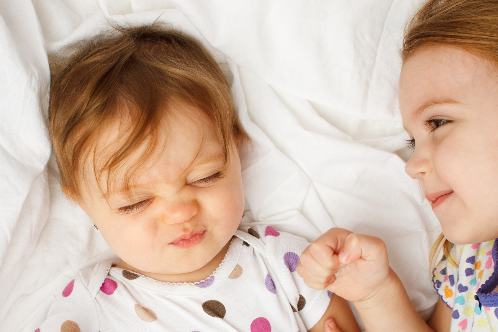 Silly baby in sheets with big sister