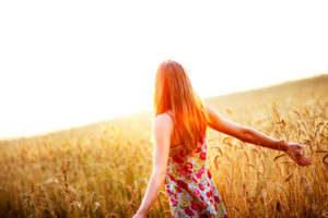 Young woman enjoying sunlight with raised arms in straw field