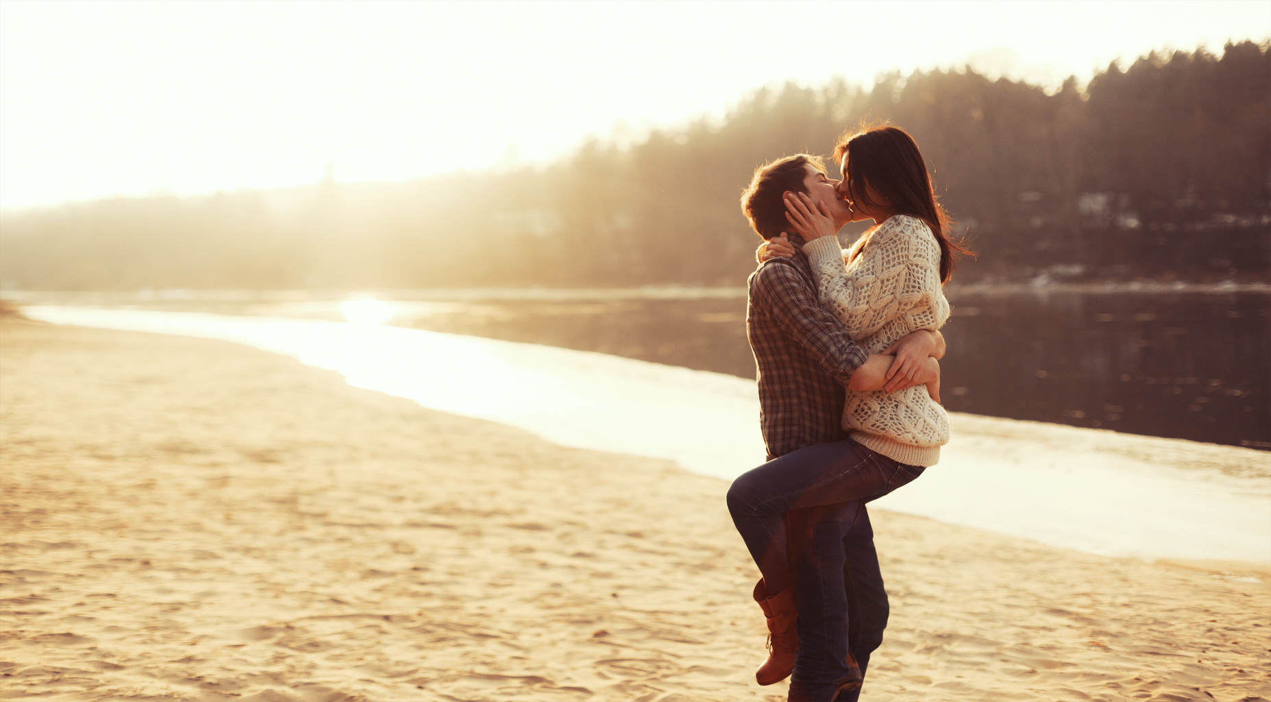 Young beautiful couple in love kissing on the beach on sunset