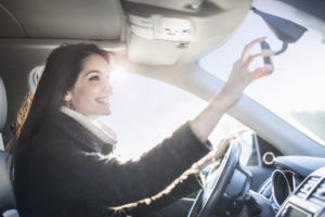 young woman looking in the rearview mirror of a car