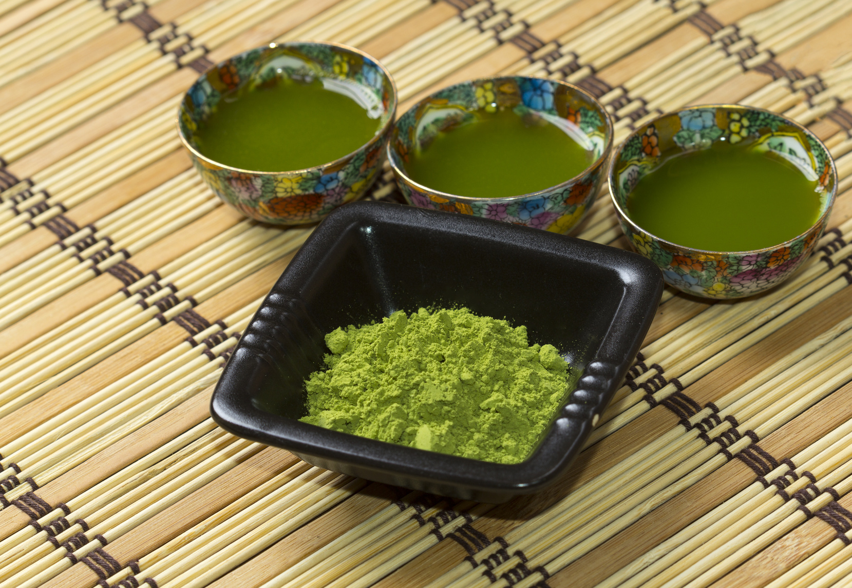 Green matcha in a small ornamented cups and black plate