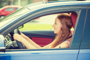 Happy beautiful young woman driving her new blue car