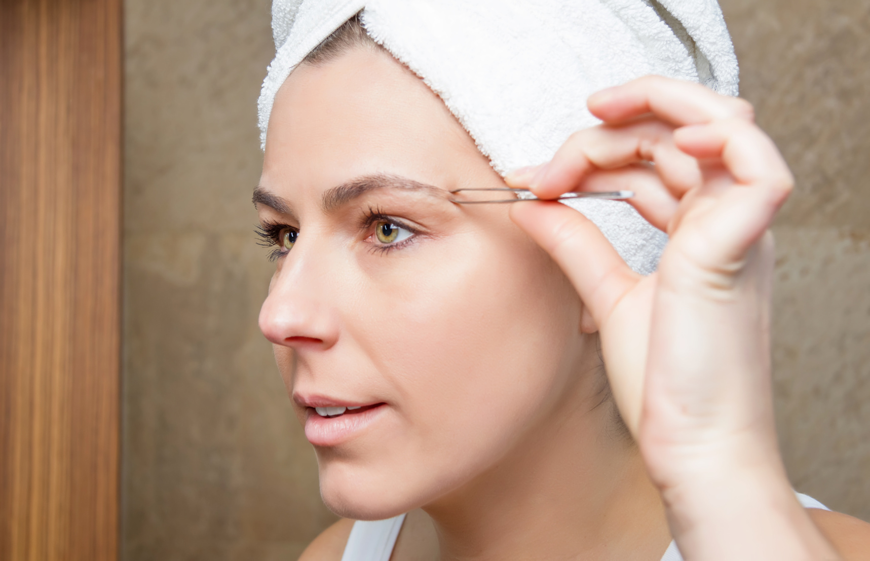 Portrait of girl plucking eyebrows with tweezers