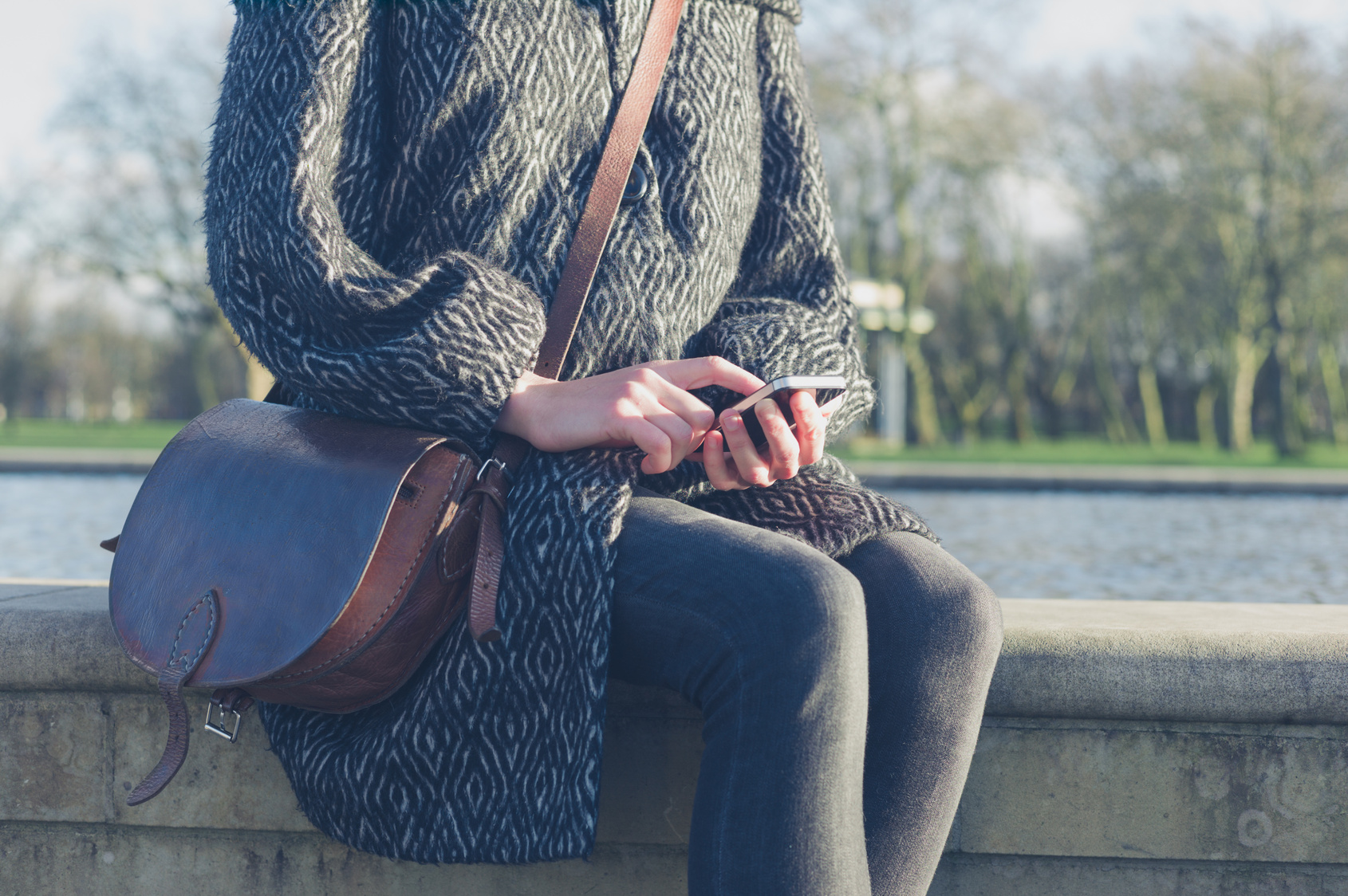 Woman using her phone by water in park