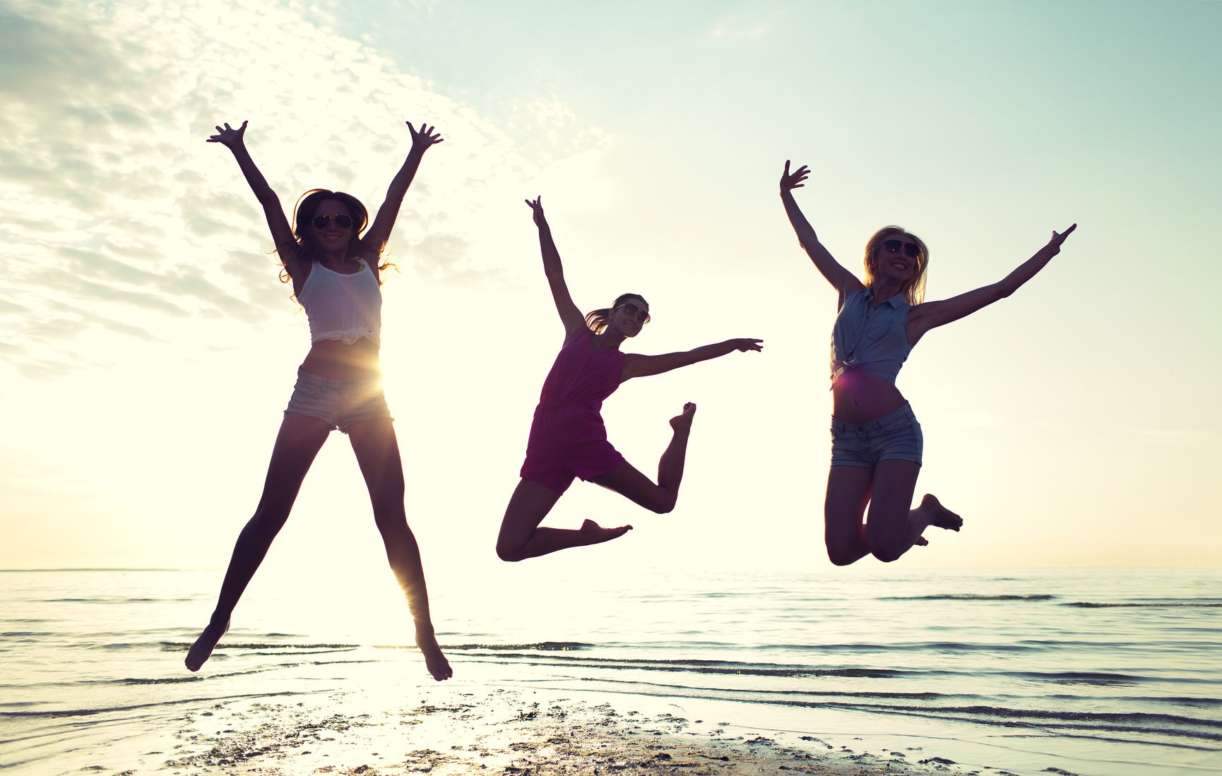 happy female friends dancing and jumping on beach