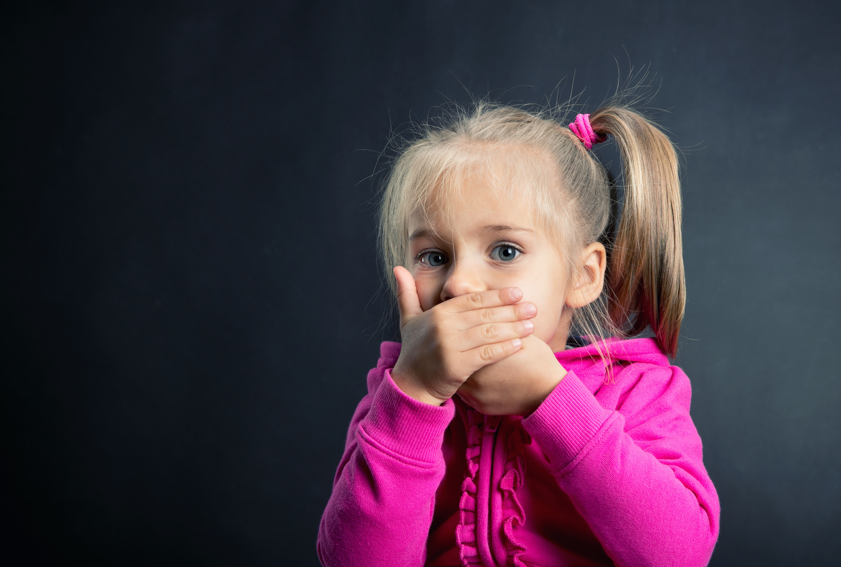 Little girl covers her mouth with hands