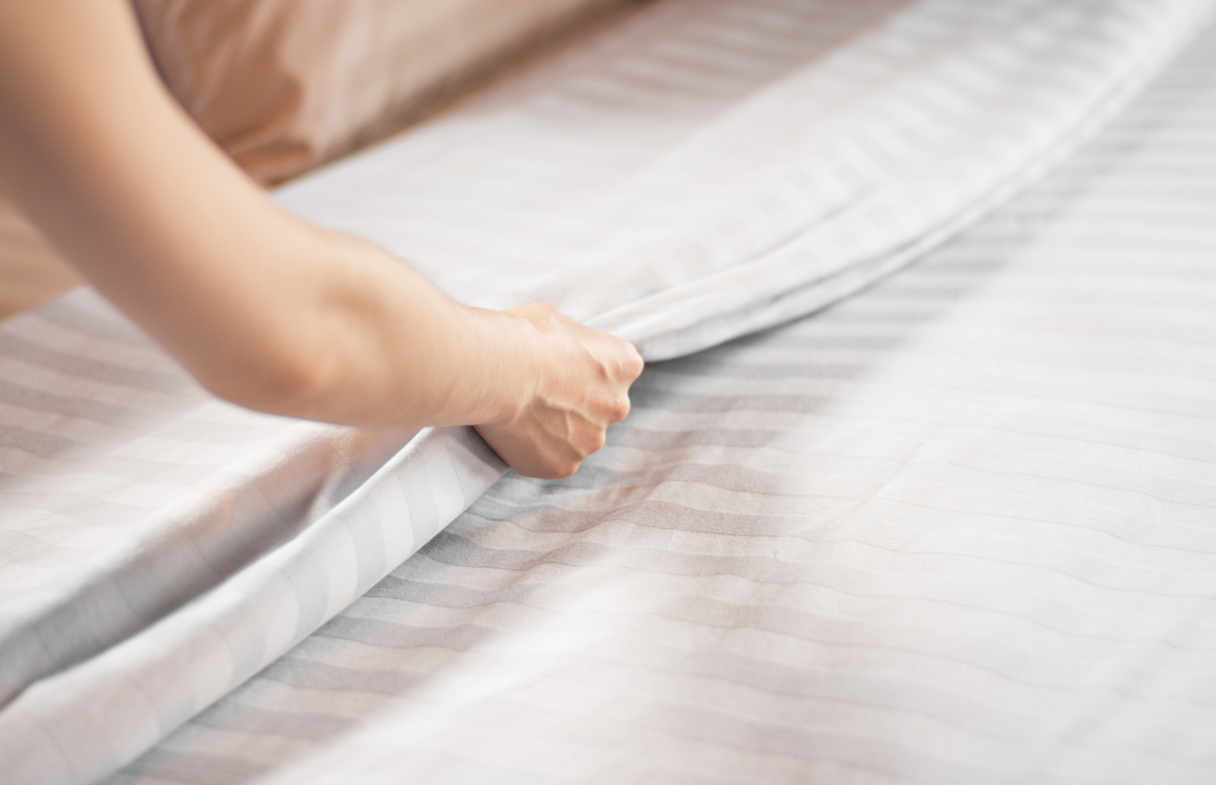 Close up woman hand set up white bed sheet in hotel room making bed