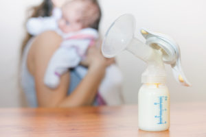 Manual breast pump and milk at background