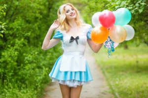 Portrait of a beautiful young blonde woman with long hair dressed as Alice in Wonderland.Girl posing with a big bunch of colorful balloons. Soft focus