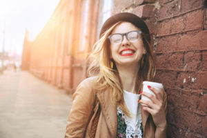 Cheerful woman in the street drinking morning coffee in sunshine light