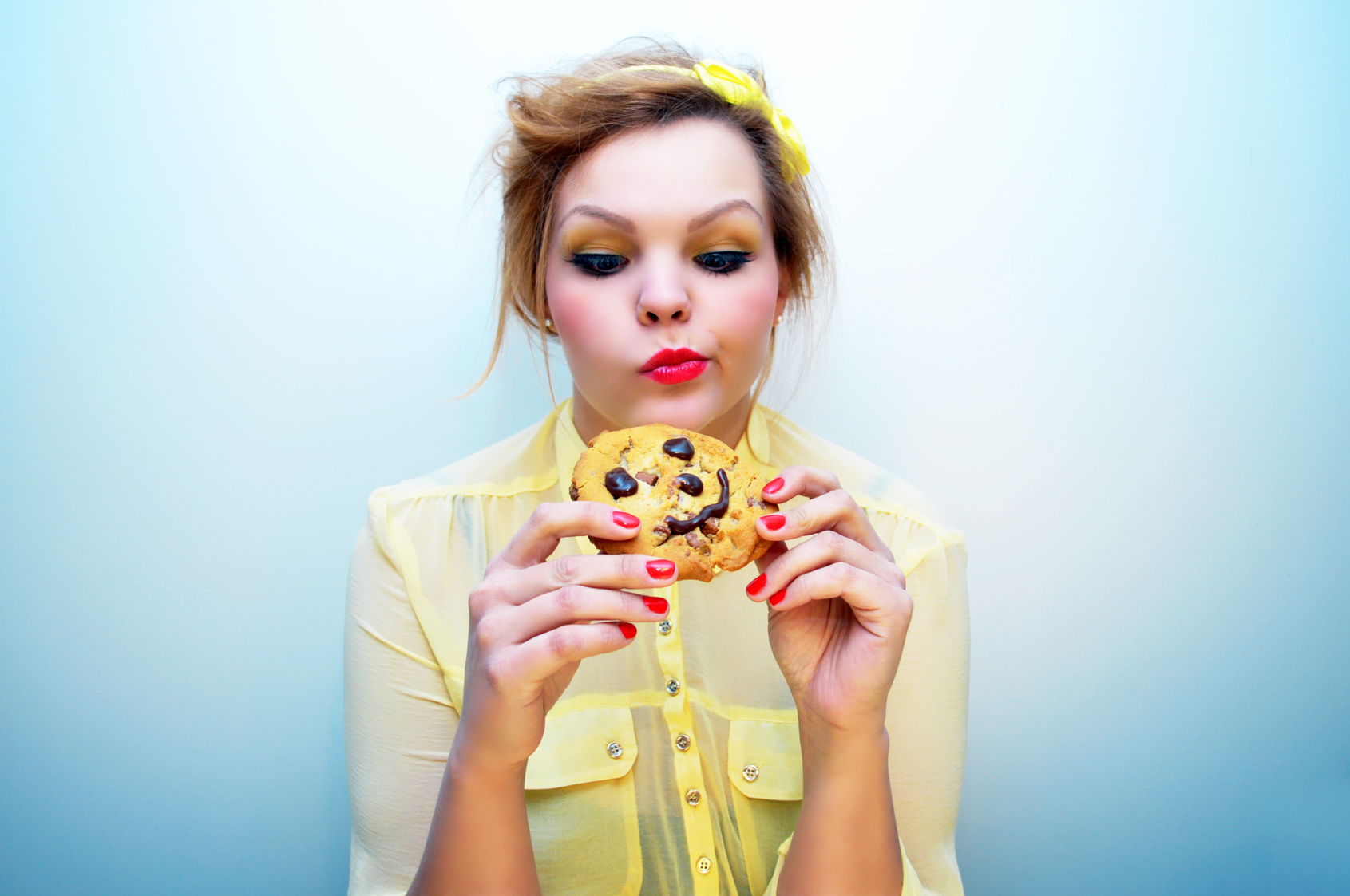 Trendy young woman is eating a smiling chocolate chip cookie.