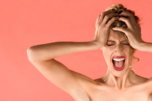 Portrait of gorgeous blonde female holding head and screaming