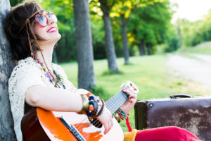 young woman sitting on a field and playing guitar