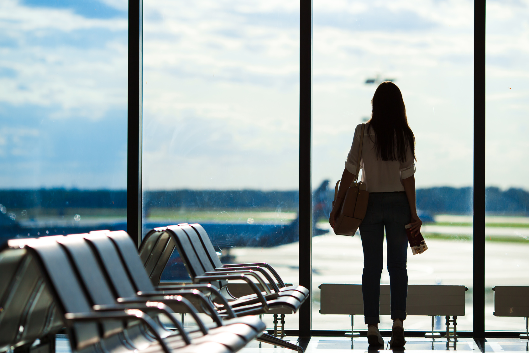 Young woman near window in an airport lounge waiting for flight aircraft