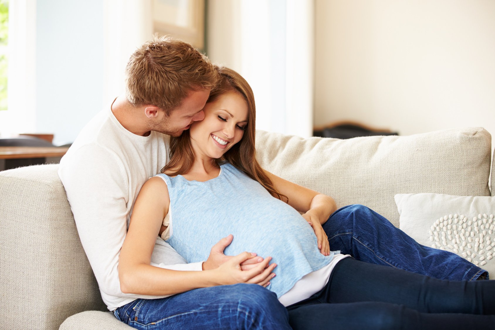 Couple With Pregnant Woman Relaxing On Sofa Together