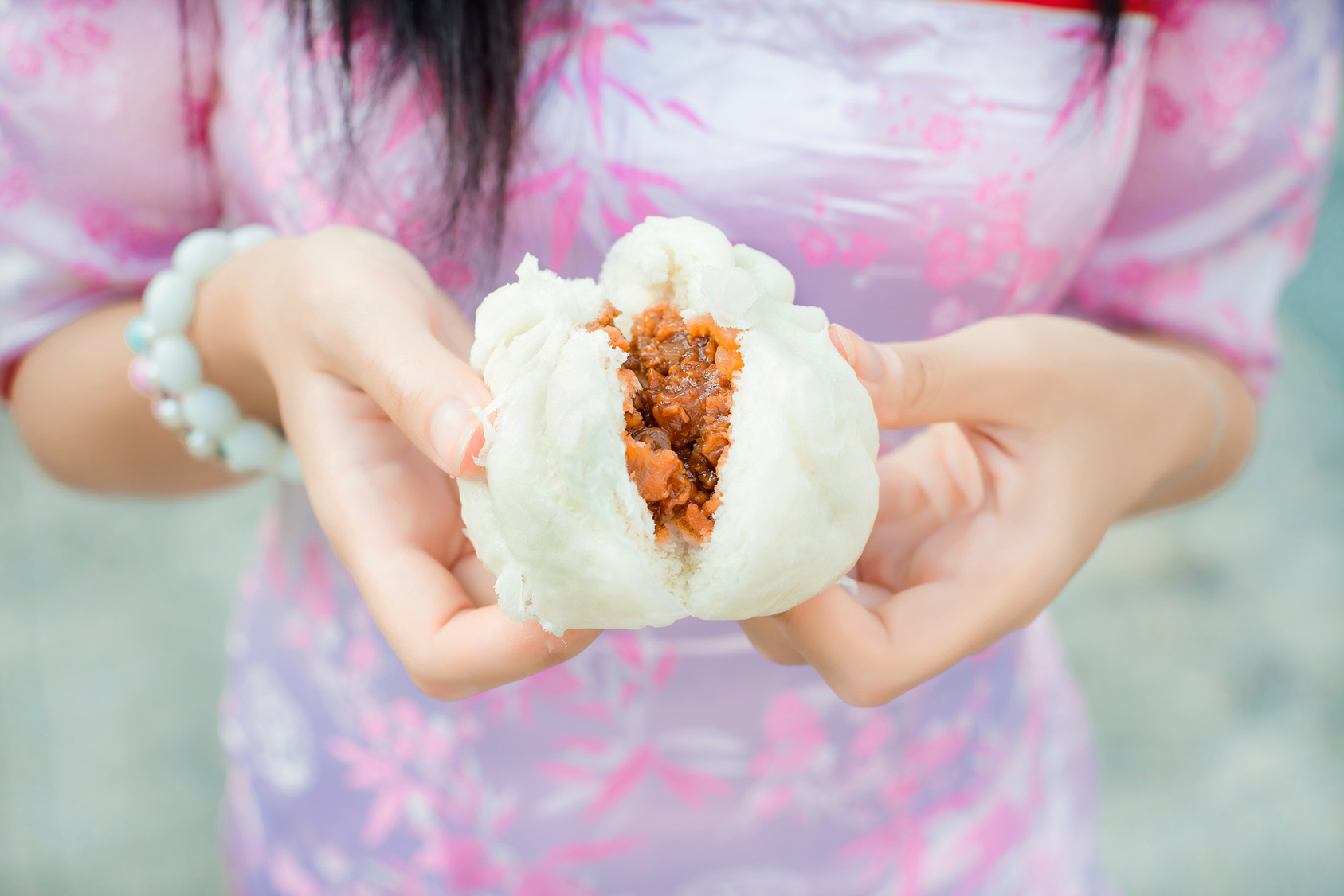 Chinese girl in cheongsam is tearing steamed stuff bun. Steamed