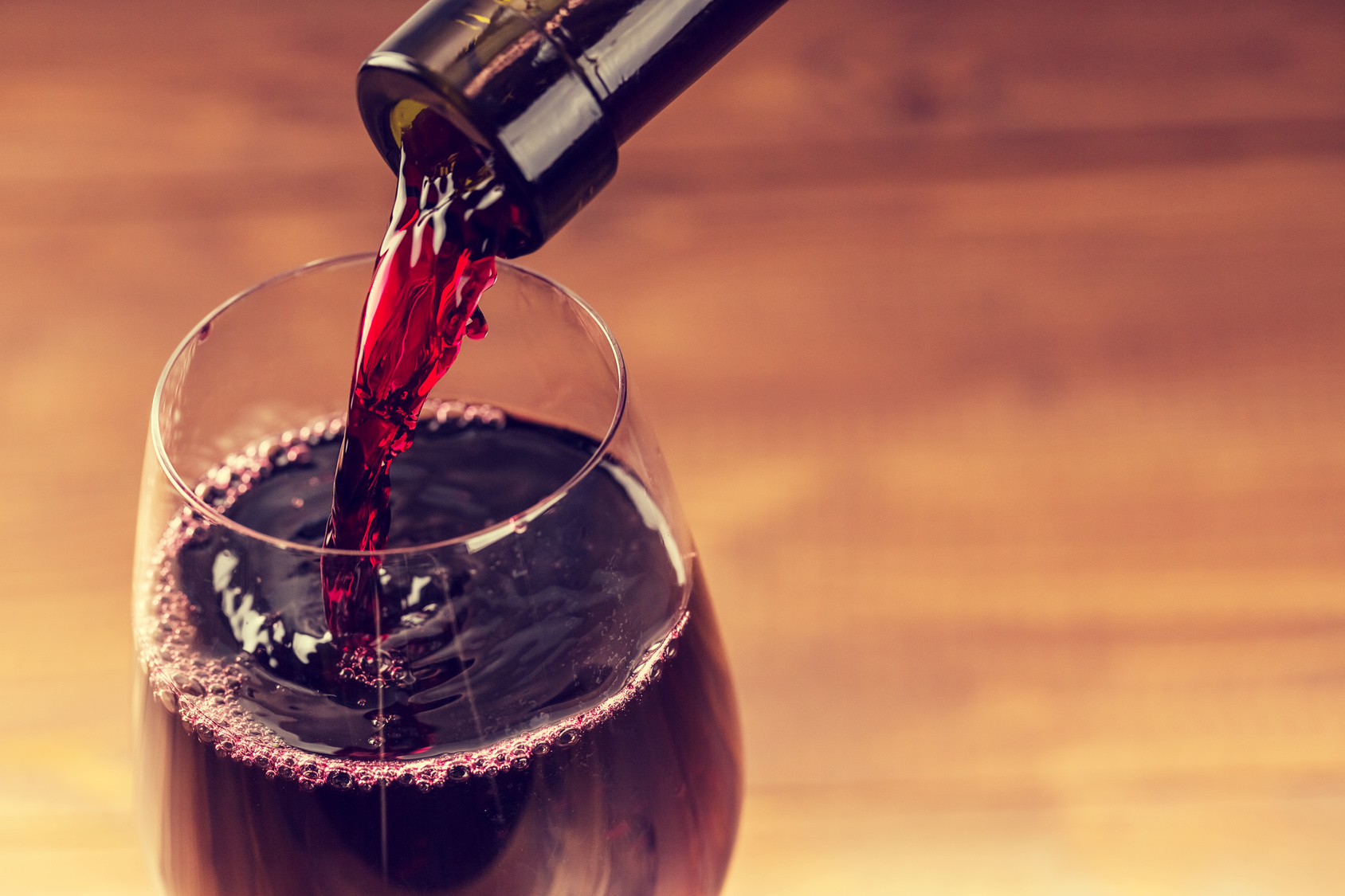 Pouring red wine into the glass against wooden background alcohol