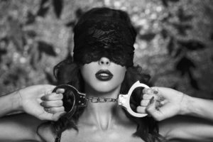 Sexy woman in lace eye cover holding handcuffs black and white