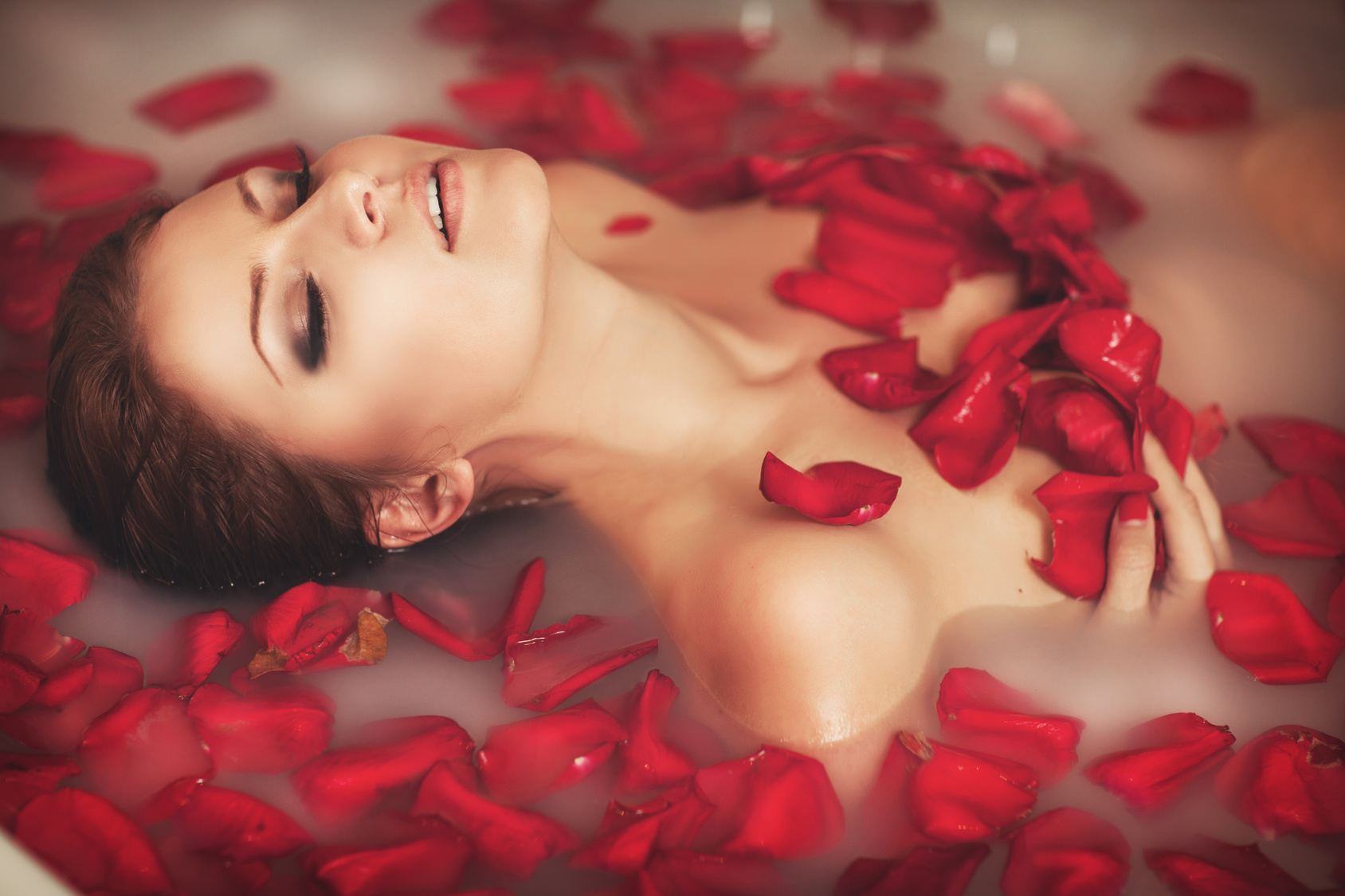 Woman in bath at spa in milk with roses petals relax