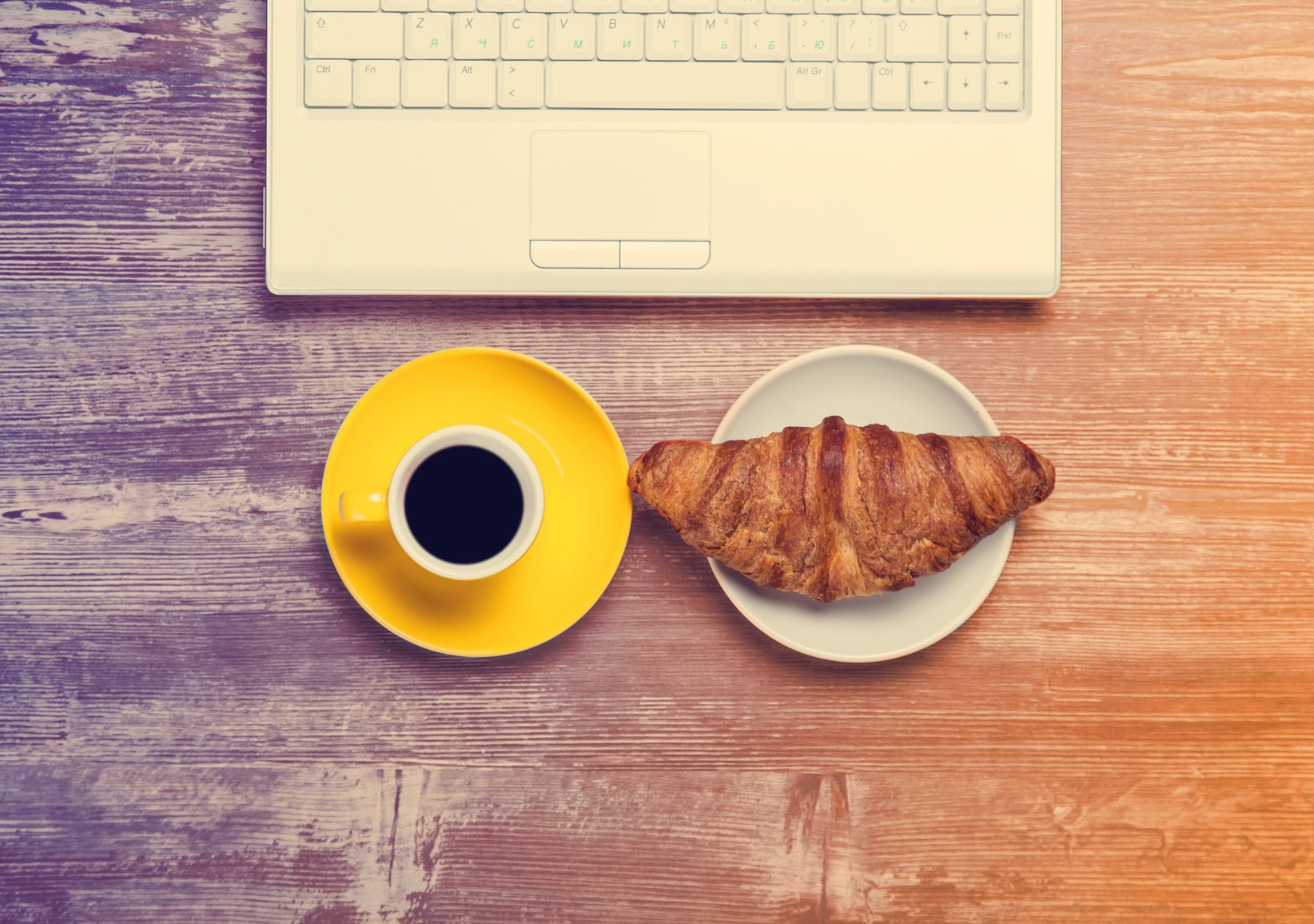 Cup of coffee and croissant near notebook on wooden table.