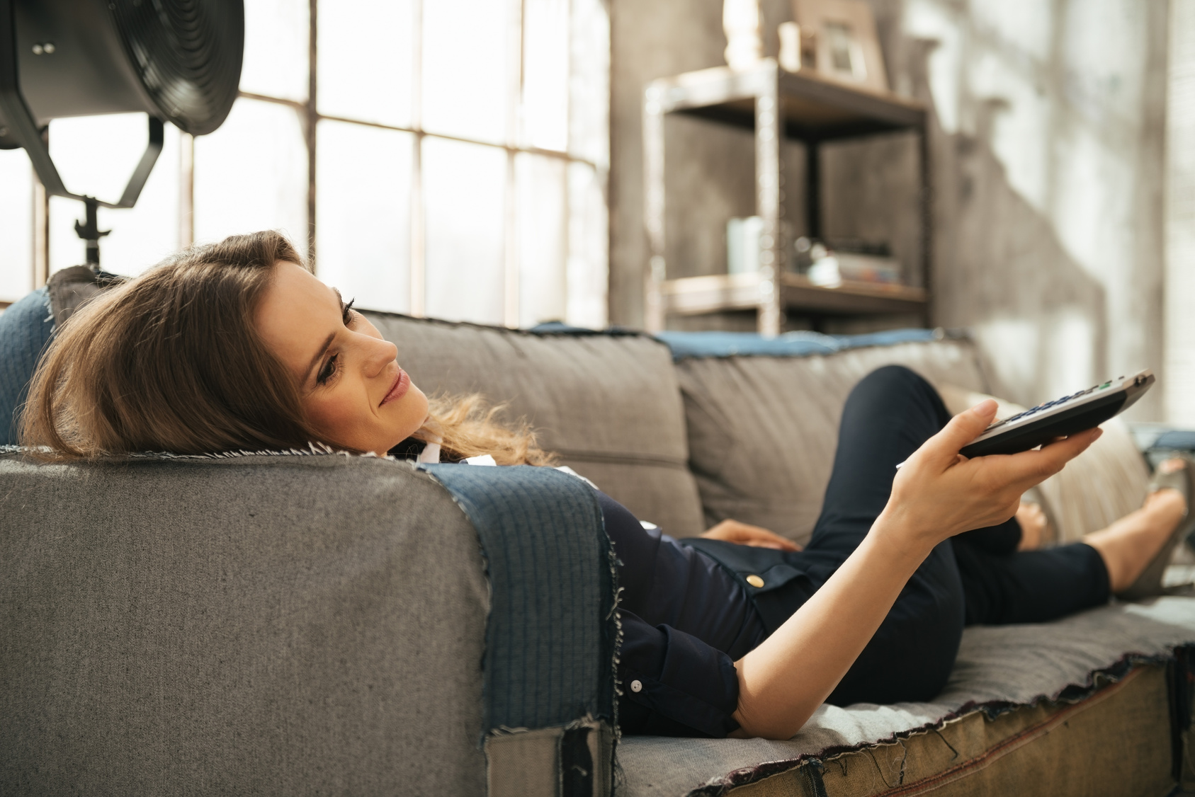 Relaxed woman lying on sofa and watching tv in loft apartment