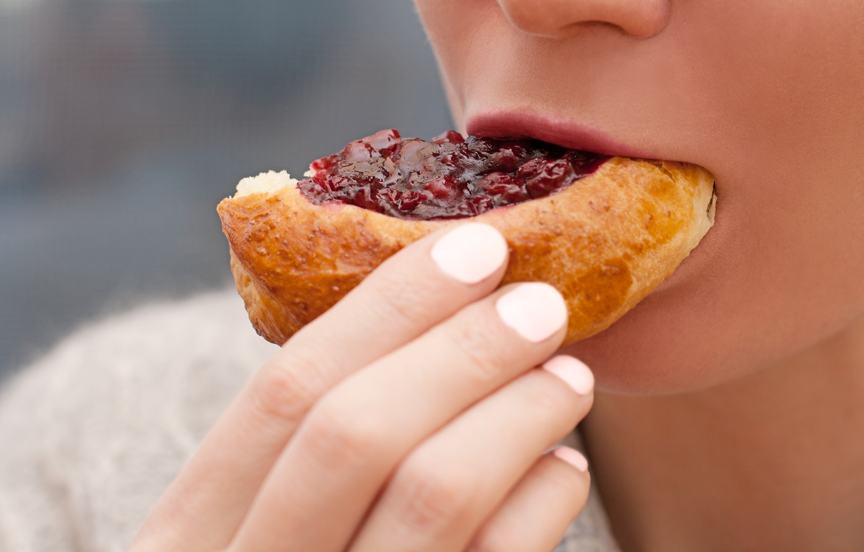 Mouth of a young woman eating pie with red jam