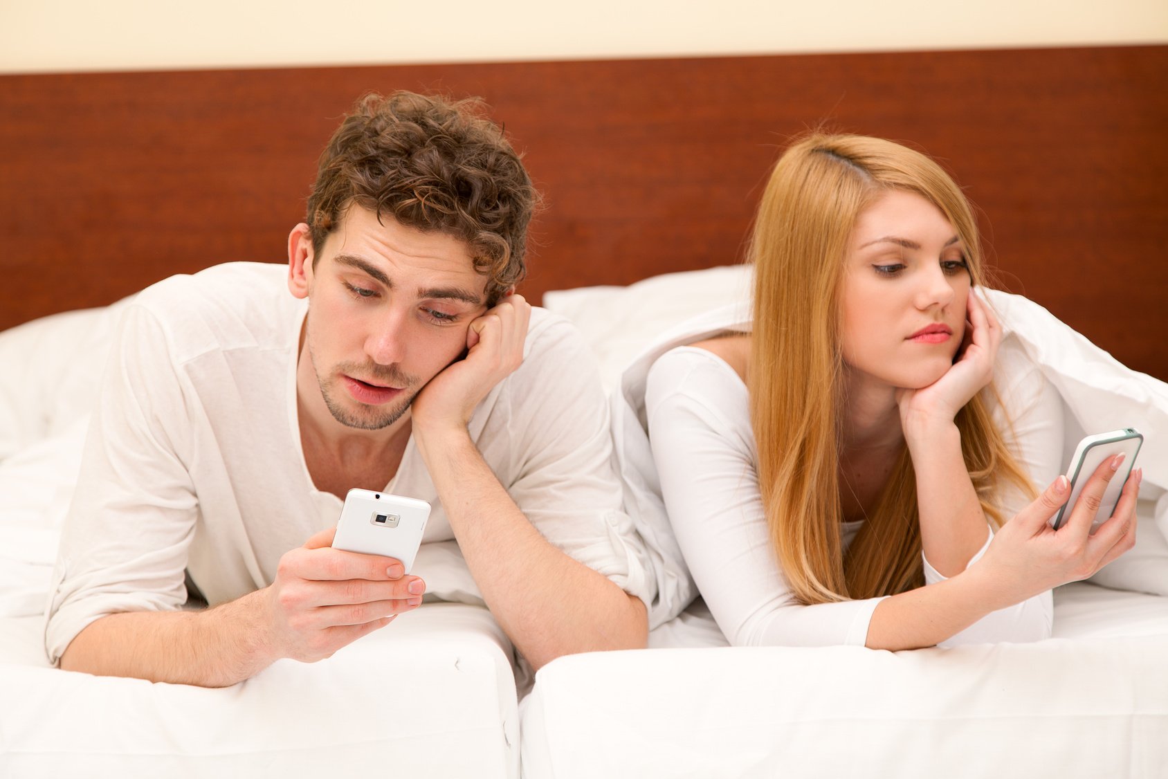 Young couple with smartphones in bed