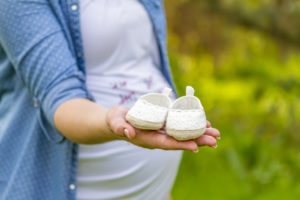 Close up of pregnant woman hand with baby shoes.