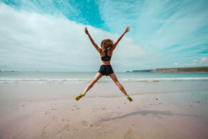 Young woman doing star jumps on the beach