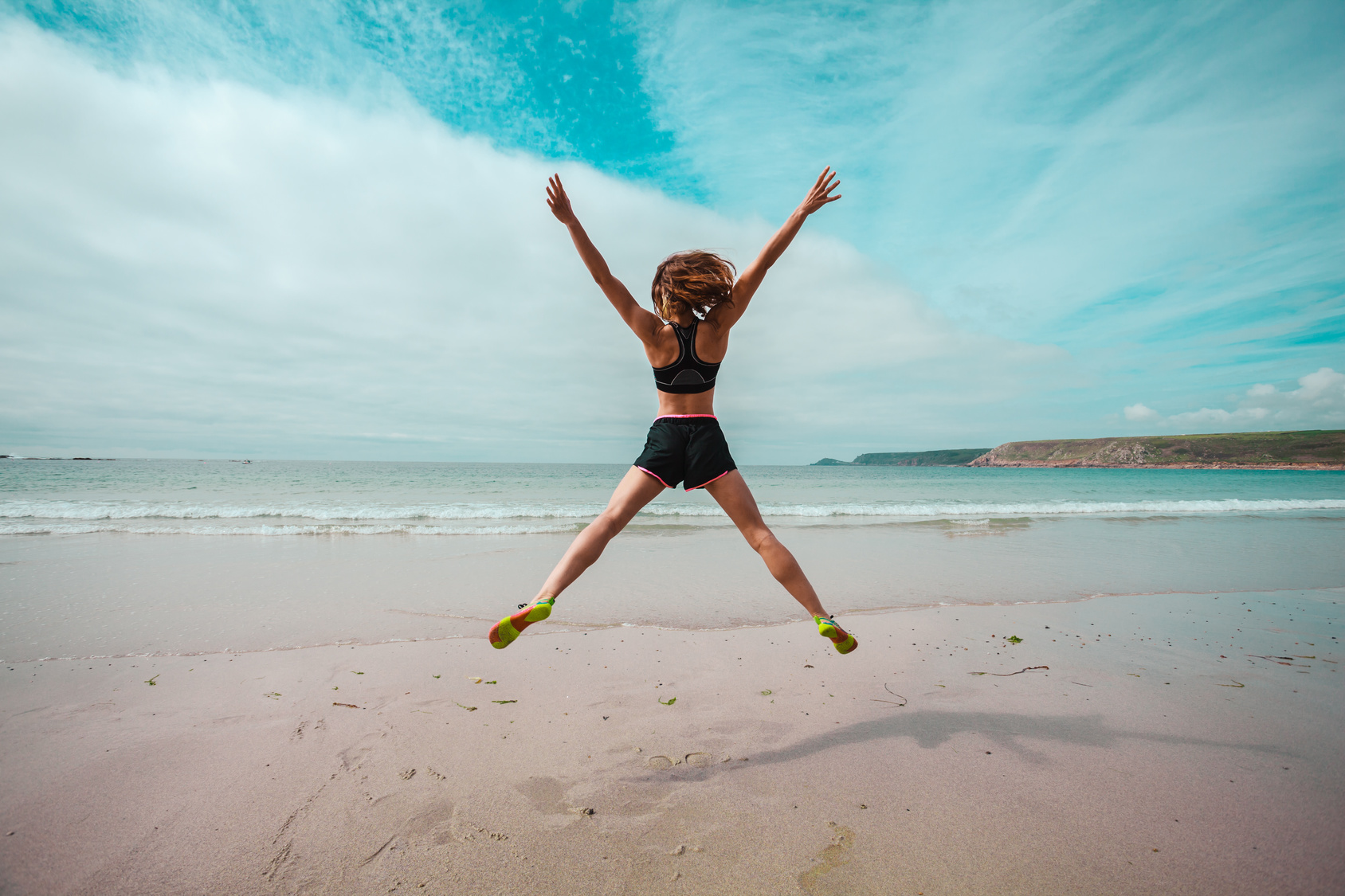 Young woman doing star jumps on the beach