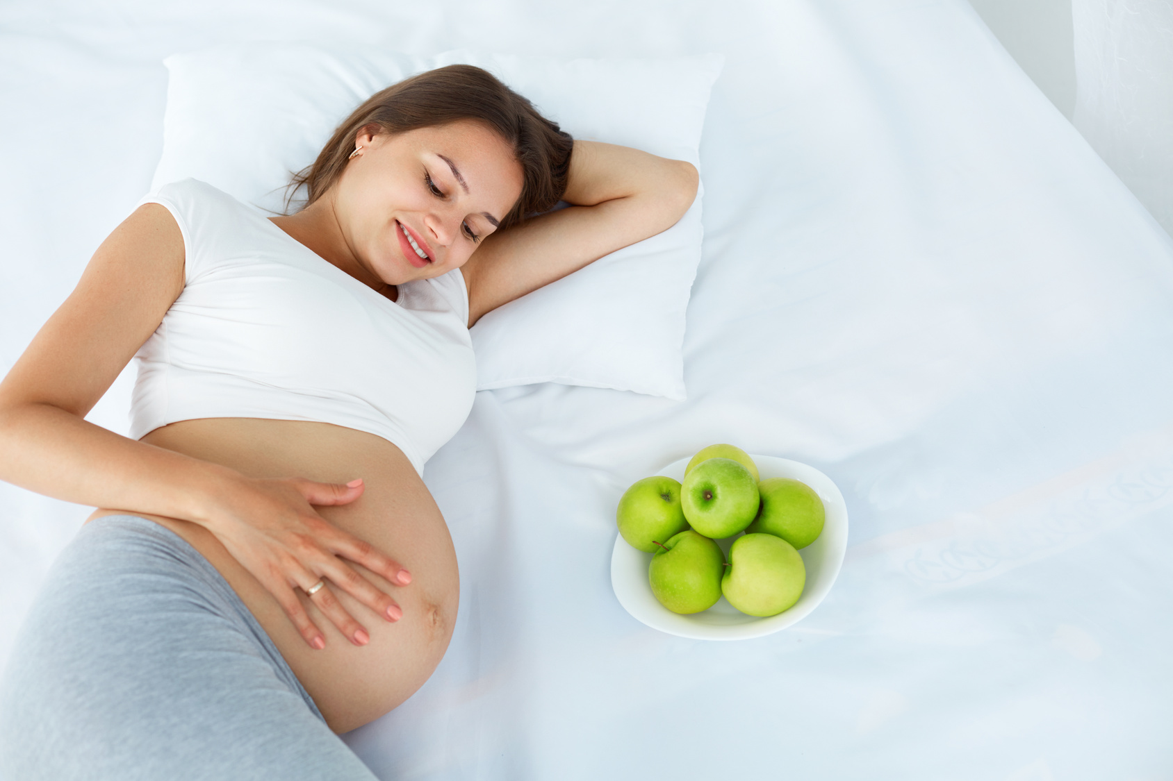 Pregnant Woman lying on the Bed with fresh Apples. Healthy Food