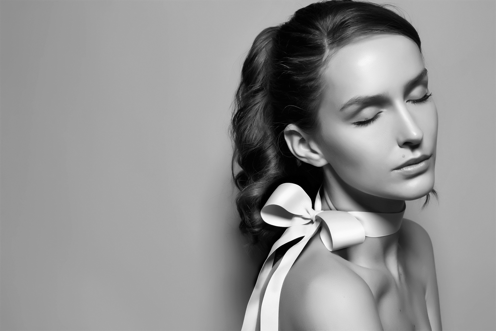 Black and white fashion portrait of Beautiful gentle brunette woman with silk bow on the sholder, shooted from the side or profile