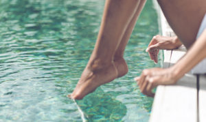 Young Woman Sitting at Poolside with Toes on Water