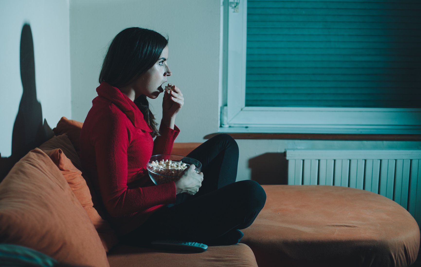 Young woman watching a horror movie and eating popcorn