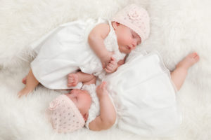 Cute twin sisters, newborn babies lying together in white dresses