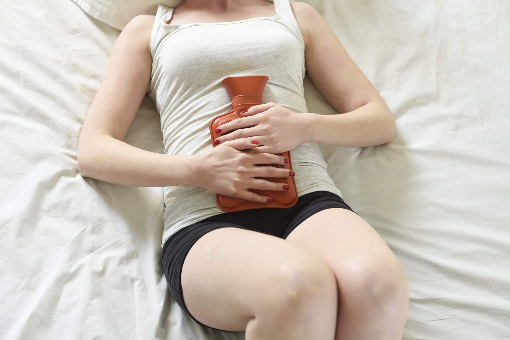 young woman suffering stomach cramps on belly holding hot water bottle against tummy