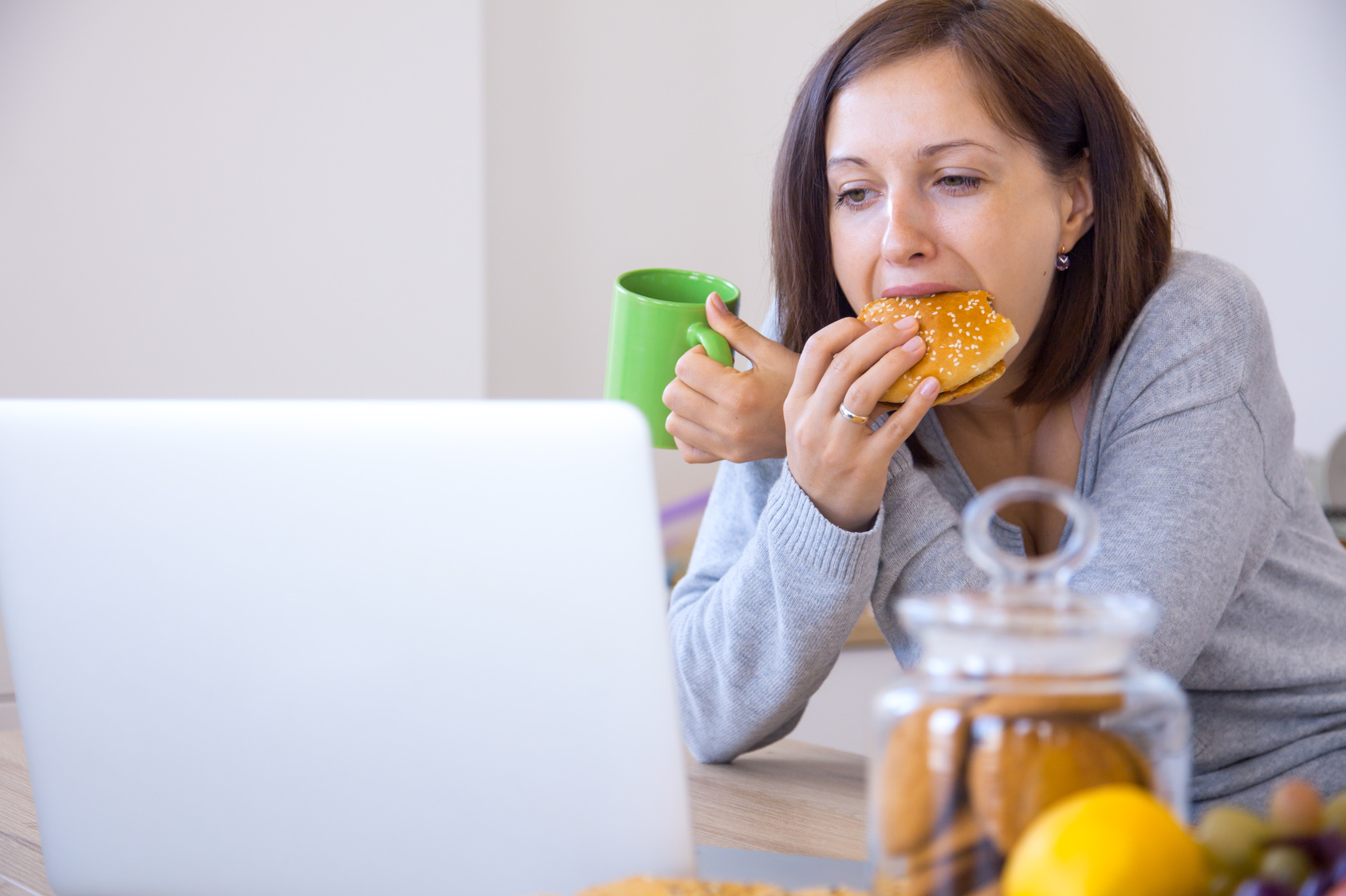 Woman eats hamburger at the workplace on kitchen